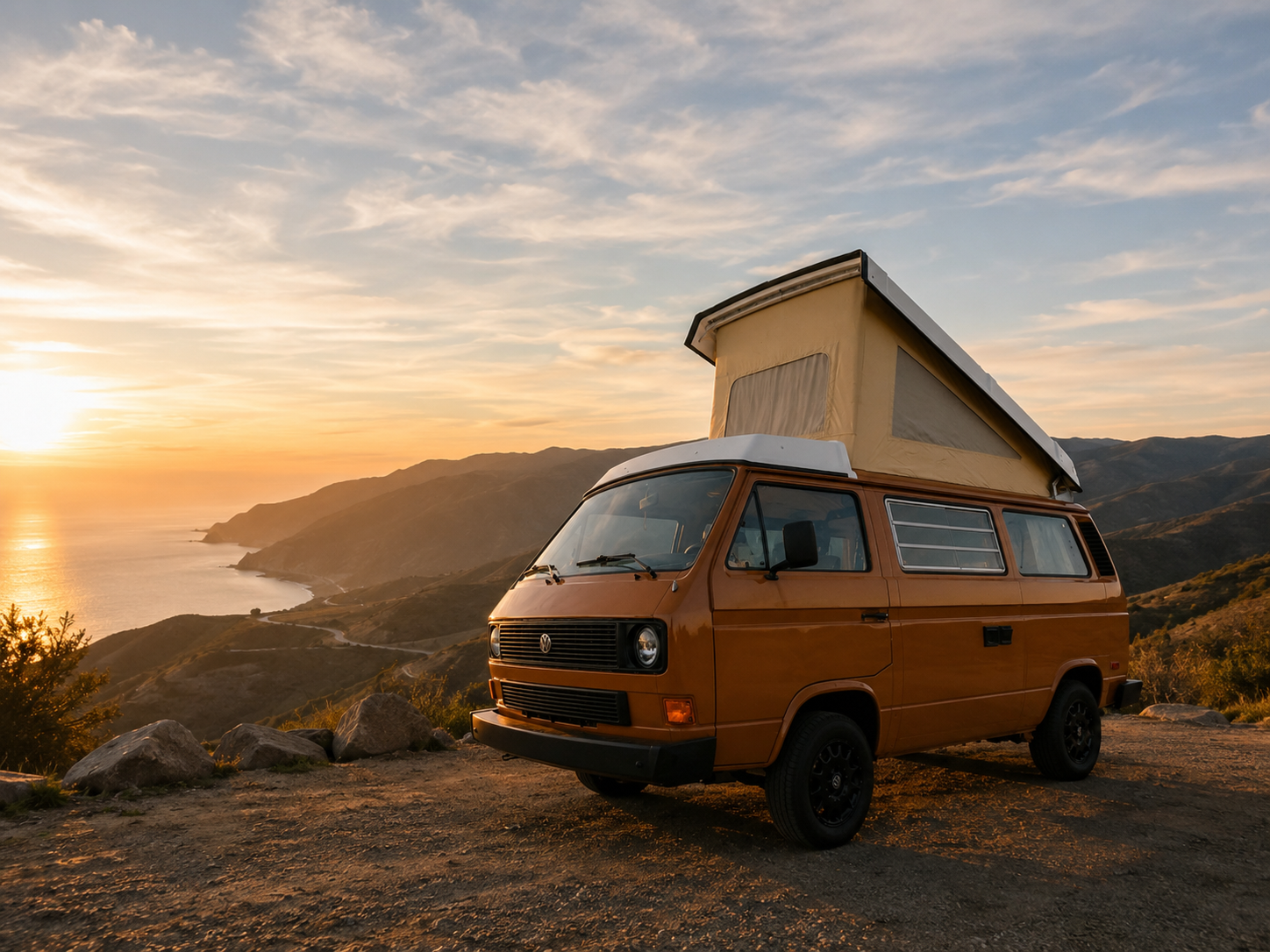 Orange Volkswagen Westfalia overlooking a coastal mountain road at sunset